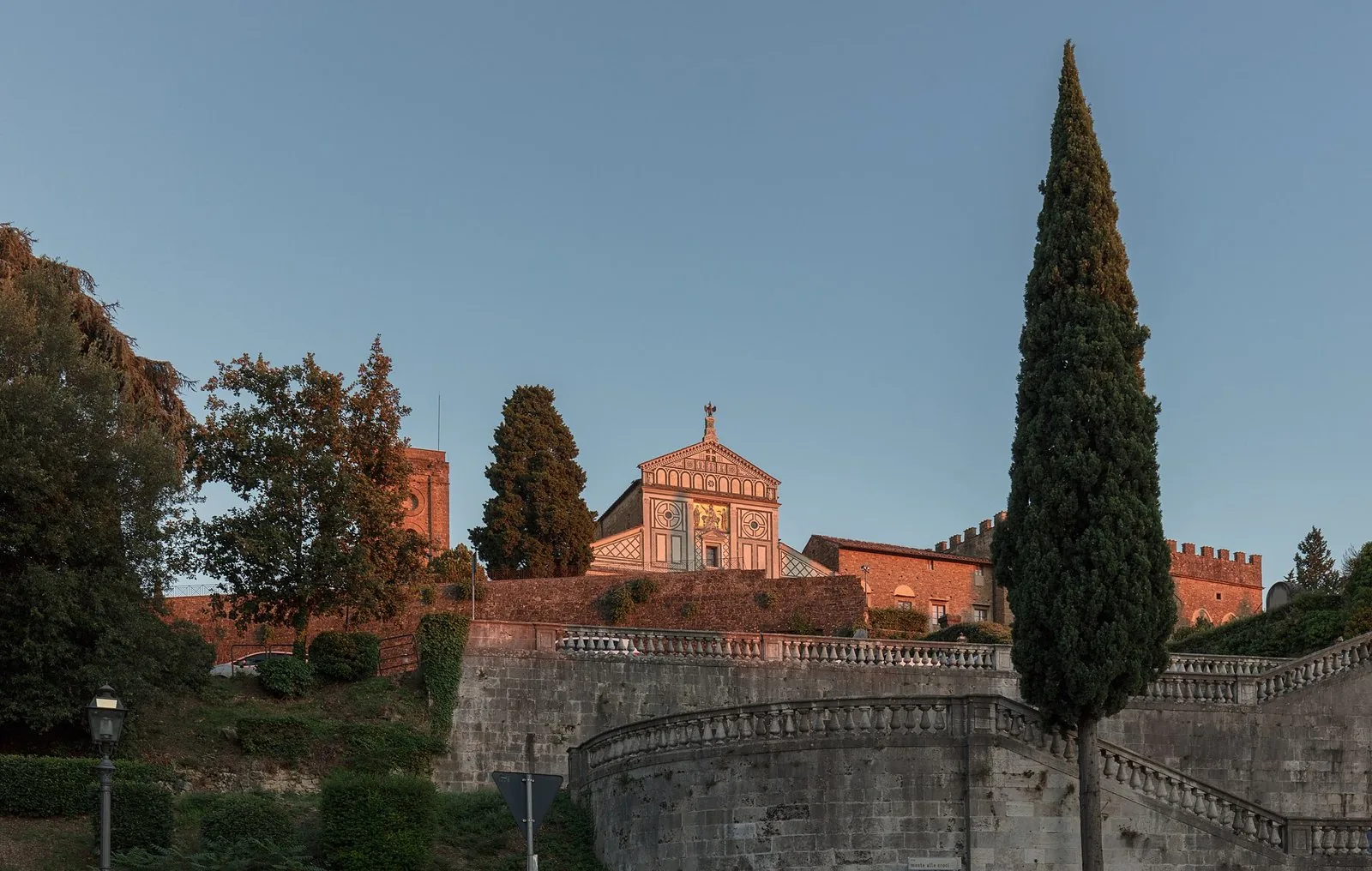 La facciata in marmo bianco e verde di San Miniato al Monte illuminata dal tramonto, sopra le scalinate tra i cipressi